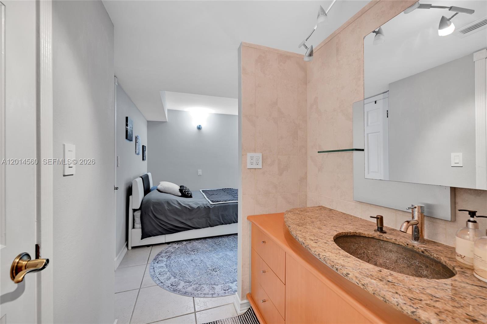 A bathroom vanity with a granite countertop sits adjacent to a bedroom with a bed — 6039 Collins Ave # 621, Miami Beach FL 33140, MIAMI BEACH, FL