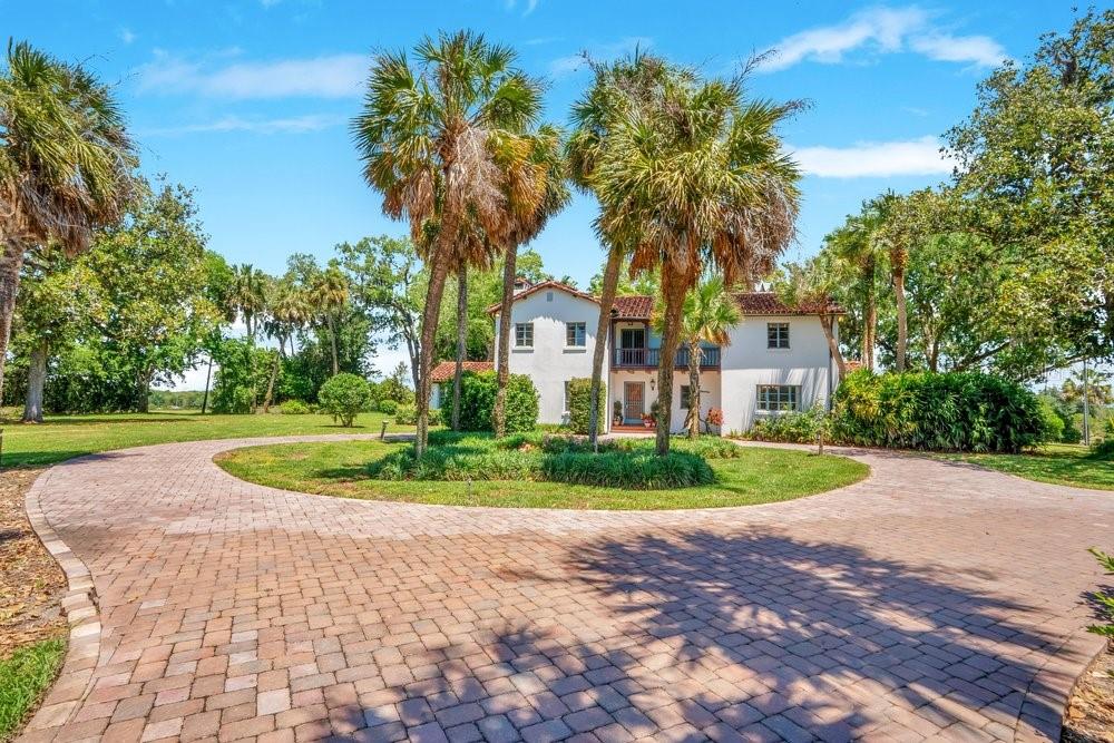 A white two-story house with a red tile roof sits behind a circular brick driveway — 14365 SE HIGHWAY 42, WEIRSDALE, FL