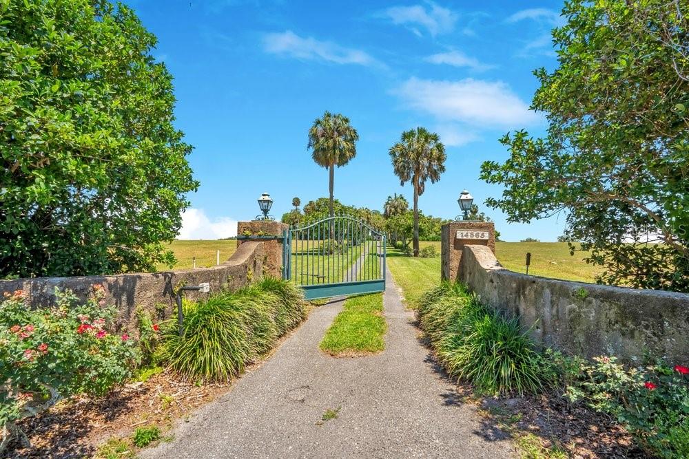 A paved driveway leads through a green metal gate between two stone pillars — 14365 SE HIGHWAY 42, WEIRSDALE, FL