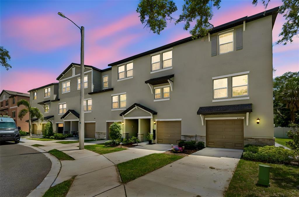 A three-story townhouse exterior features tan stucco, gray siding, and three attached garages — 4436 TUSCAN LOON DRIVE, TAMPA, FL