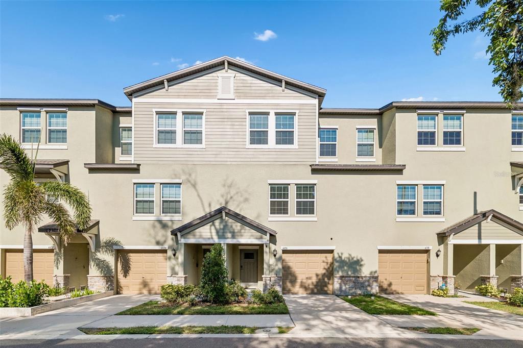 The exterior of a two-story townhouse features a tan stucco facade, stone accents, and a garage — 4436 TUSCAN LOON DRIVE, TAMPA, FL
