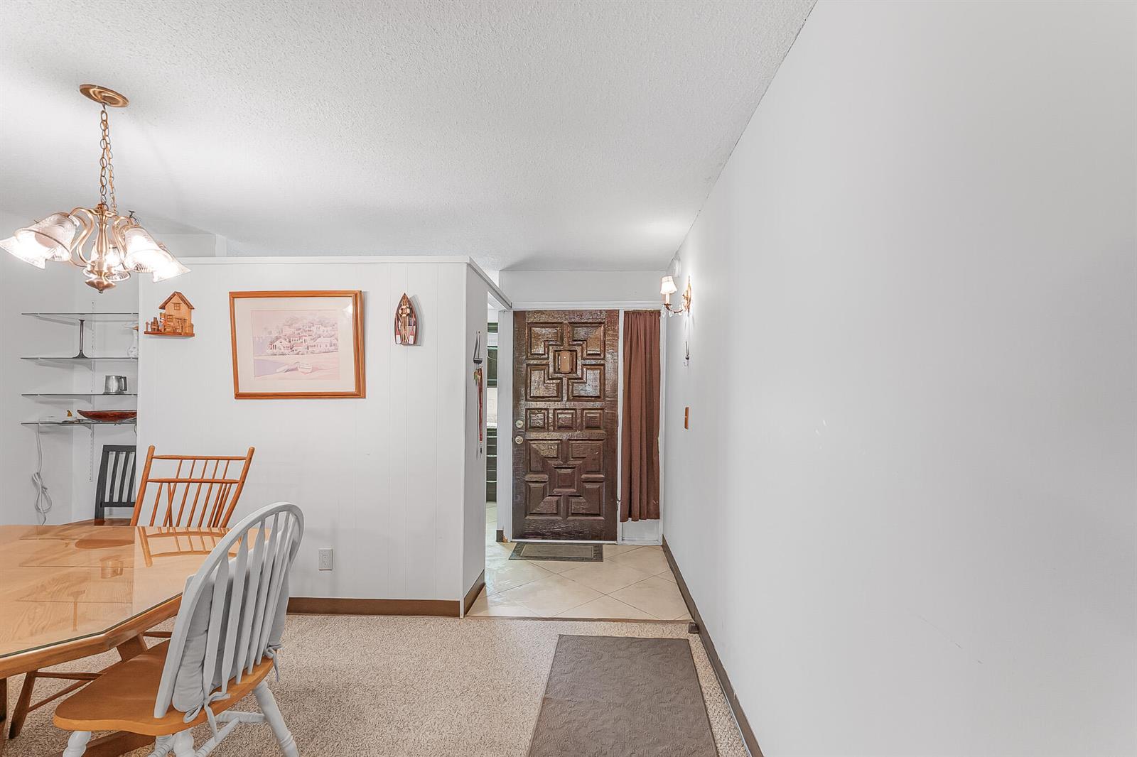 A dining area with carpeted floors leads to an entryway with a decorative wooden door — 1500 NE 13th Terrace # G6, Jensen Beach FL 34957, JENSEN BEACH, FL