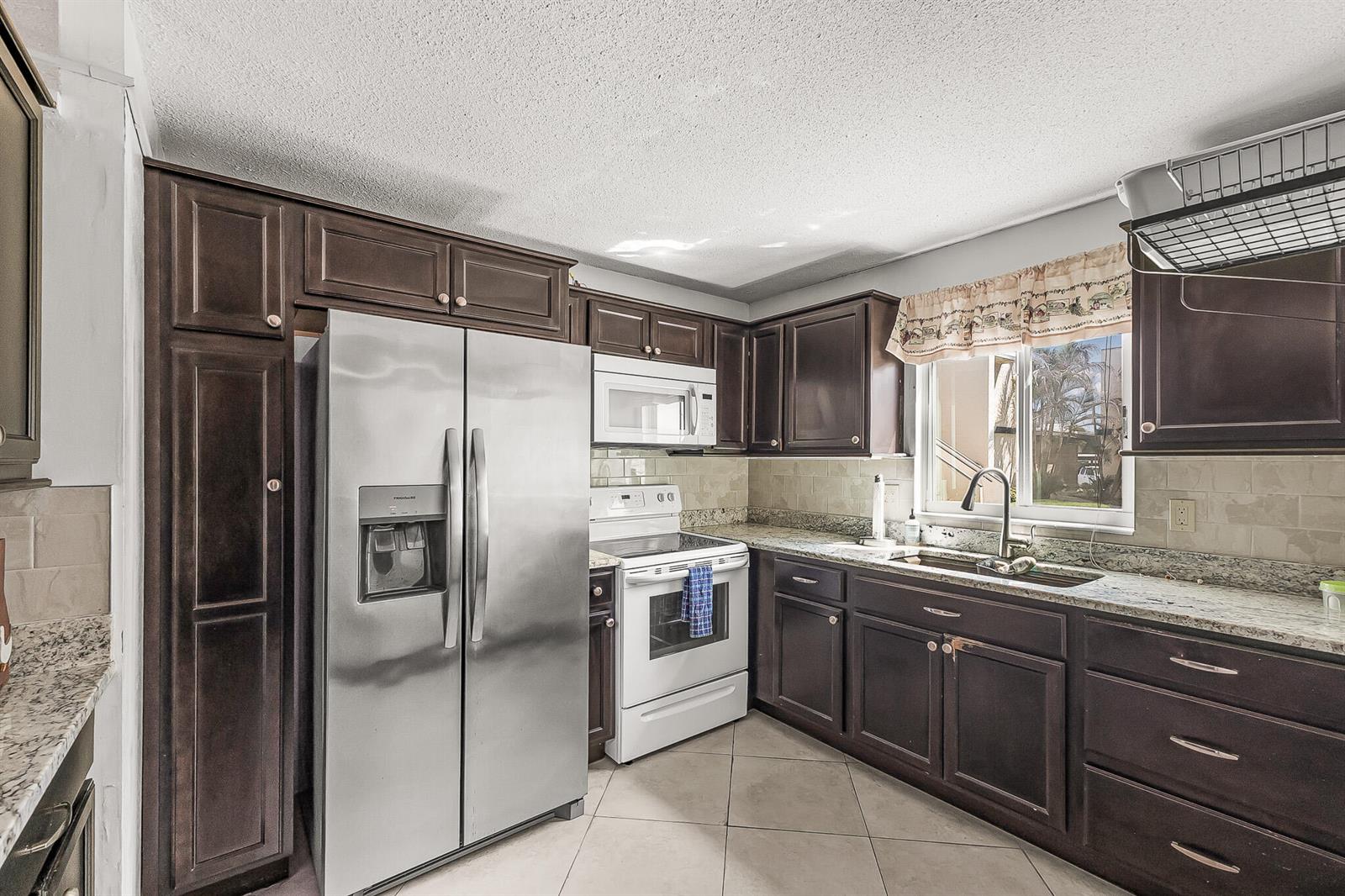 A kitchen features dark wood cabinets, stainless steel appliances, granite countertops, and tile flooring — 1500 NE 13th Terrace # G6, Jensen Beach FL 34957, JENSEN BEACH, FL