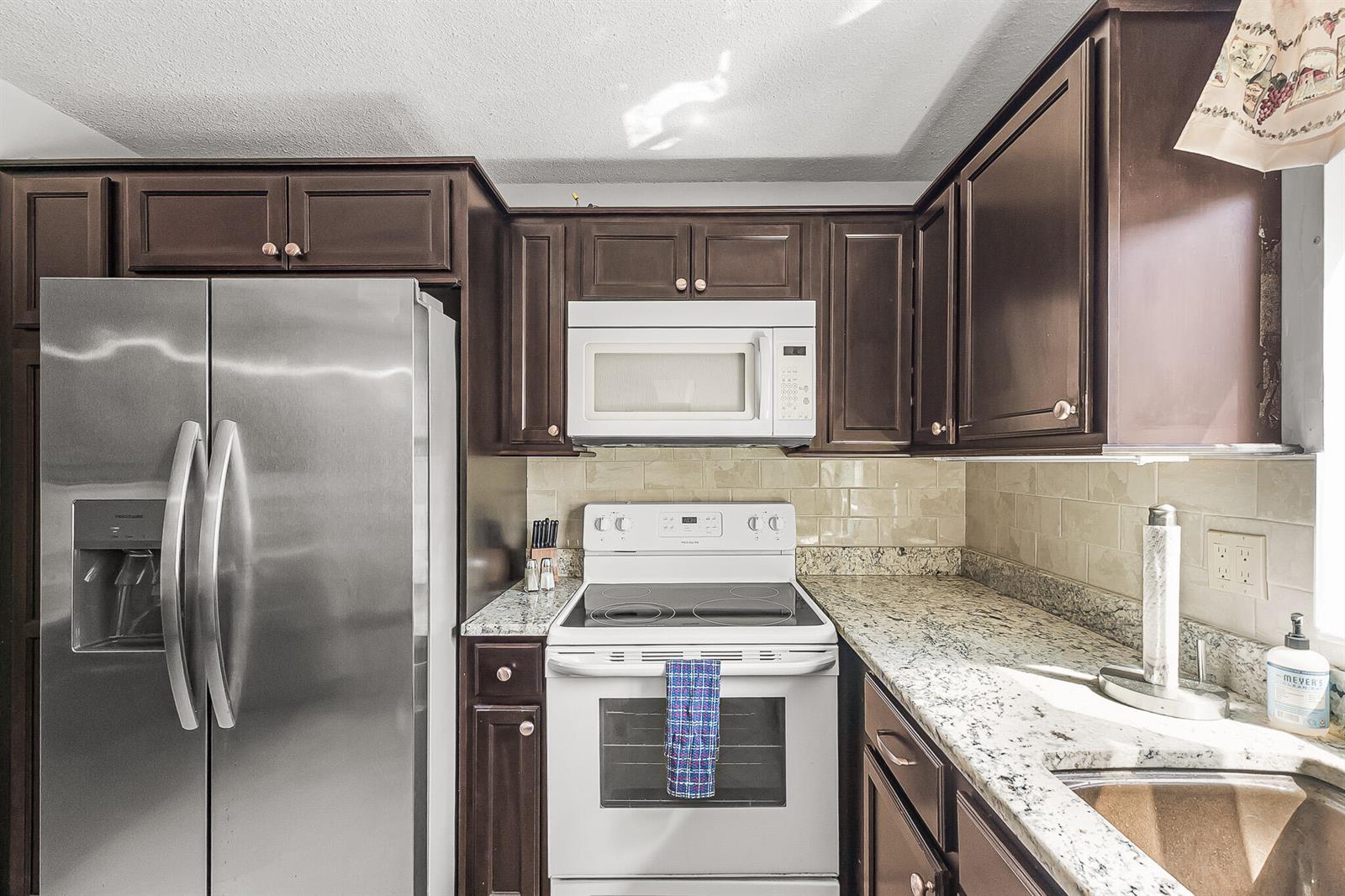 A kitchen features dark wood cabinets, granite countertops, a stainless refrigerator, and white appliances — 1500 NE 13th Terrace # G6, Jensen Beach FL 34957, JENSEN BEACH, FL