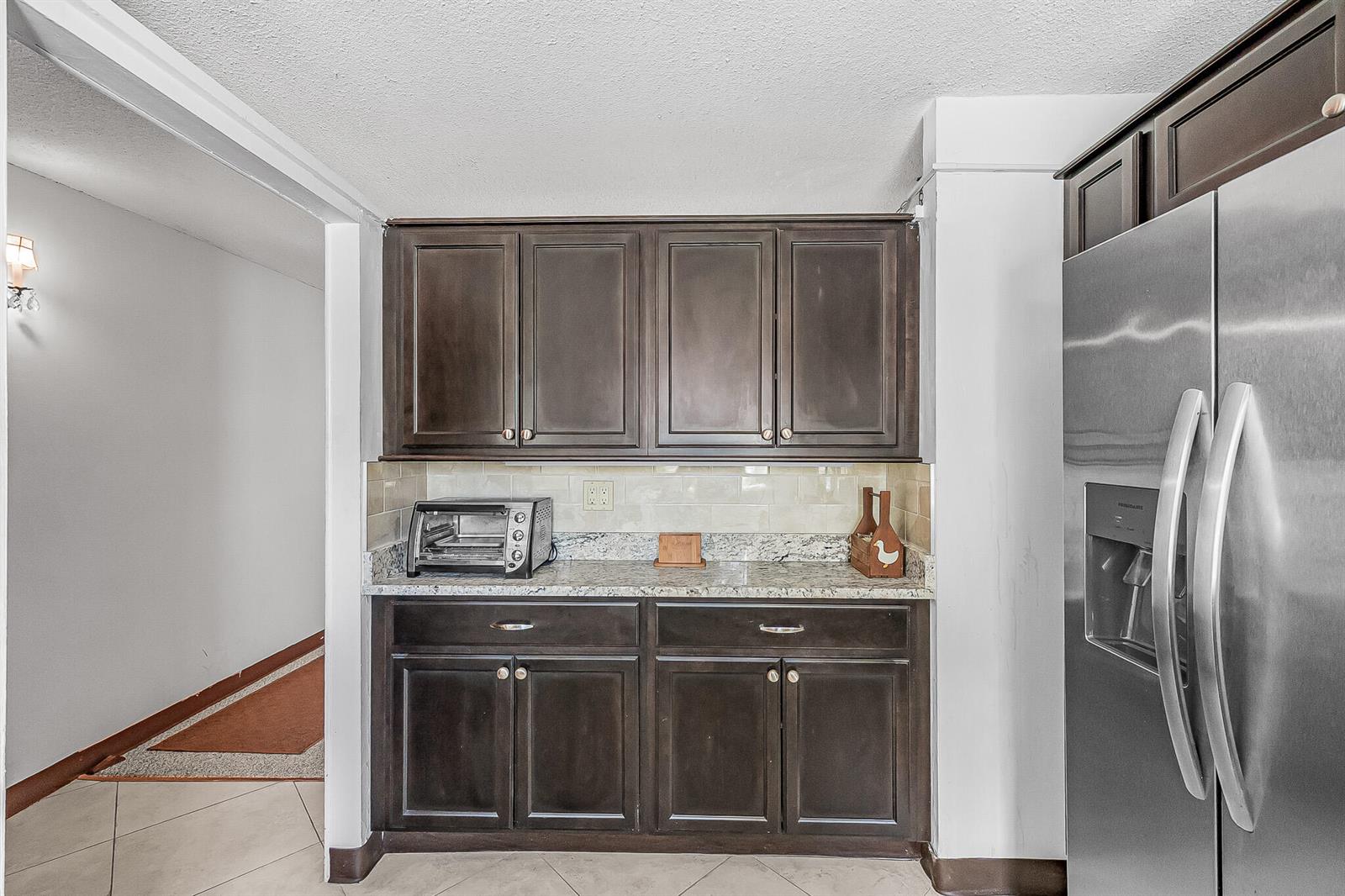 A kitchen area features dark wood cabinets, granite countertops, a tile backsplash, and stainless steel refrigerator — 1500 NE 13th Terrace # G6, Jensen Beach FL 34957, JENSEN BEACH, FL