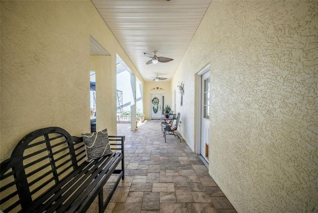 A covered outdoor patio features stone-paver flooring, a ceiling fan, and a black wooden bench — 8037 SW 81ST LOOP, OCALA, FL