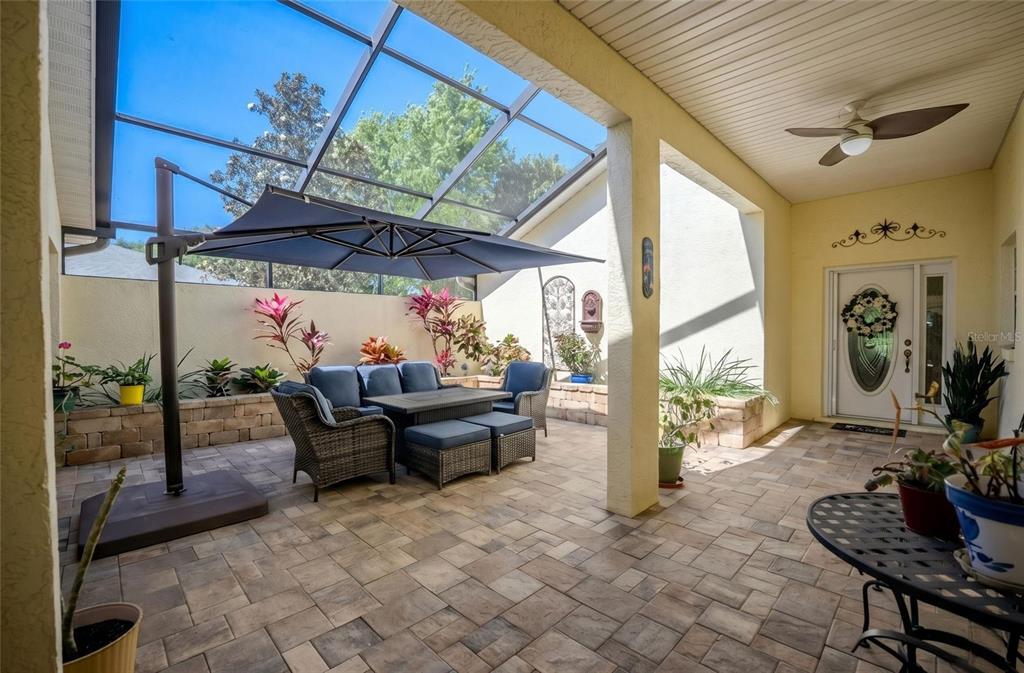 A covered patio features a screened enclosure, stone pavers, outdoor furniture, and a ceiling fan — 8037 SW 81ST LOOP, OCALA, FL