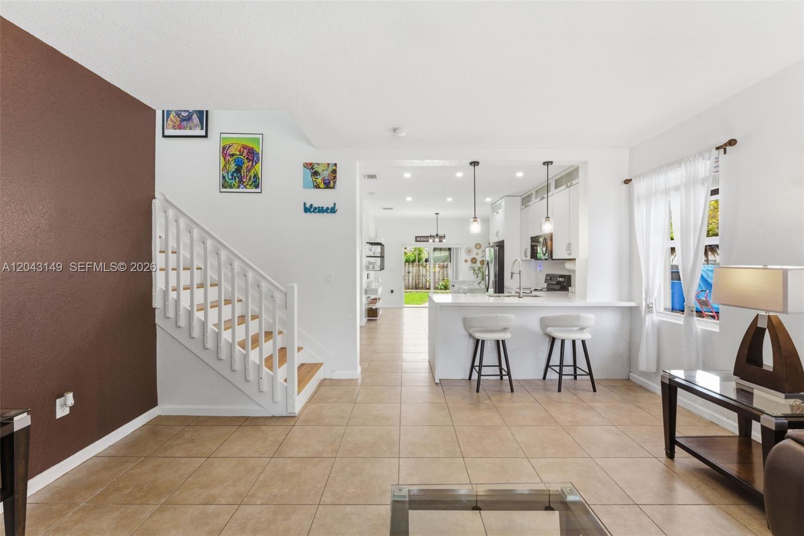 A living room with tile floors and a staircase leads to an open kitchen area — 12964 SW 285th Ter, Homestead FL 33033, HOMESTEAD, FL
