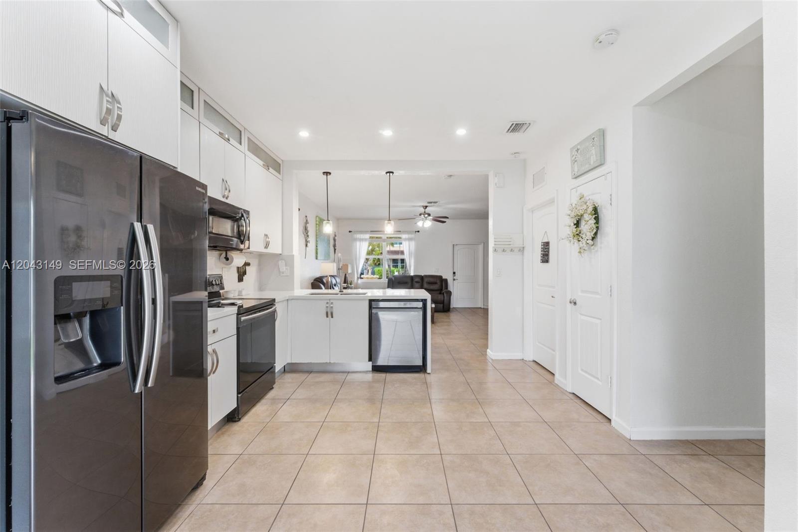 A kitchen with white cabinets, stainless steel appliances, and tile flooring leads to a living area — 12964 SW 285th Ter, Homestead FL 33033, HOMESTEAD, FL