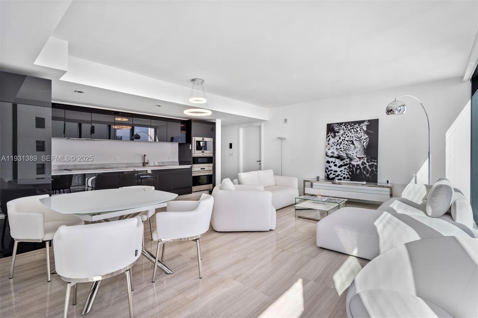 A modern open-concept living and dining area features white furniture, glossy black cabinetry, and tile flooring — 1451 Brickell Ave # 1803, Miami FL 33131, MIAMI, FL