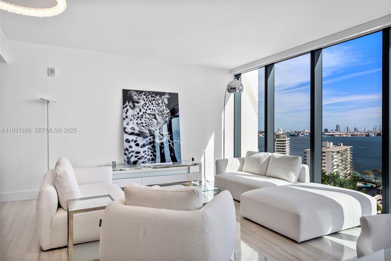 A modern living room features white furniture, a large leopard print artwork, and floor-to-ceiling windows — 1451 Brickell Ave # 1803, Miami FL 33131, MIAMI, FL