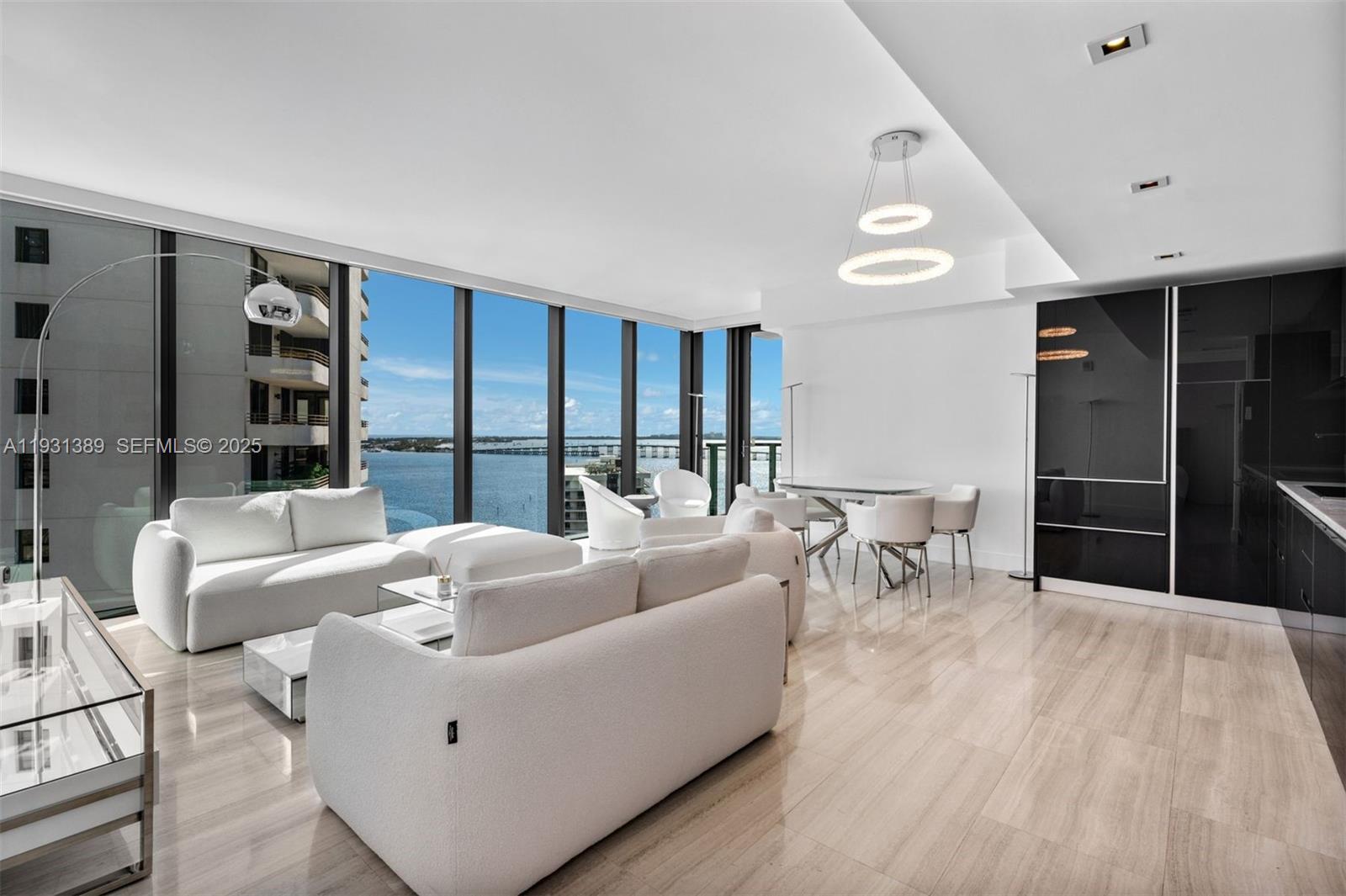 A modern living and dining area features white furniture, tile floors, and floor-to-ceiling water views — 1451 Brickell Ave # 1803, Miami FL 33131, MIAMI, FL