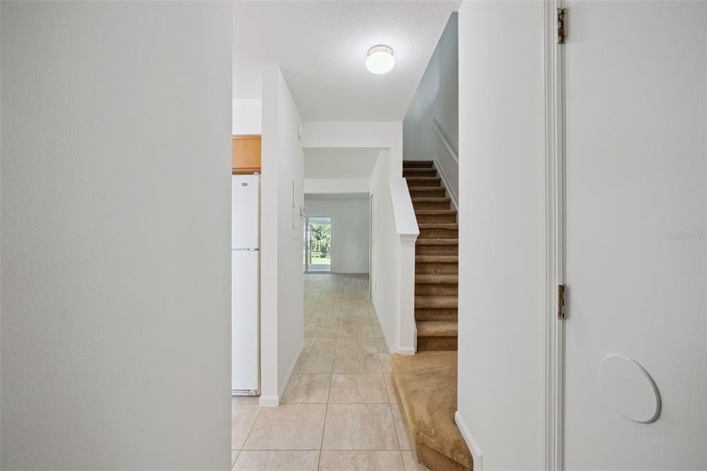 A hallway with tile flooring leads to a kitchen and stairs with brown carpet — 498 GREEN SPRING CIR, WINTER SPRINGS, FL