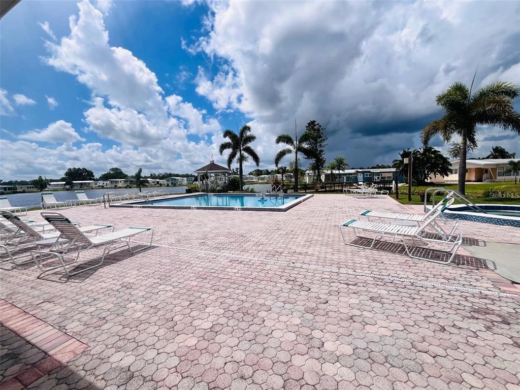 A swimming pool with lounge chairs on a paved deck overlooking a lake — 2215 73RD STREET E UNIT 348, PALMETTO, FL