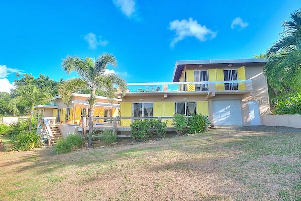 A two-story house with yellow shutters, a wooden deck, and a garage under a blue sky — 16 ALTURAS DE ZONI, CULEBRA, PR