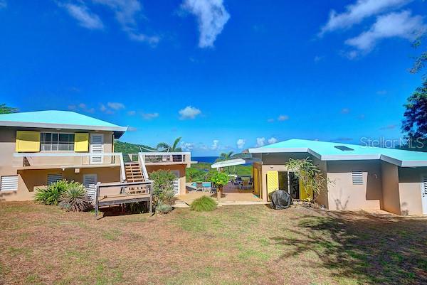 Two detached houses with light-colored walls and turquoise roofs stand on a grassy hillside — 16 ALTURAS DE ZONI, CULEBRA, PR