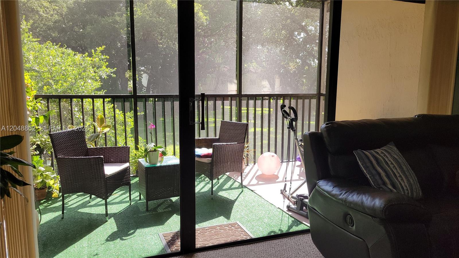 A living room looks out through a sliding glass door onto a screened-in balcony — 461 Ives Dairy Rd # 2, Miami FL 33179, MIAMI, FL