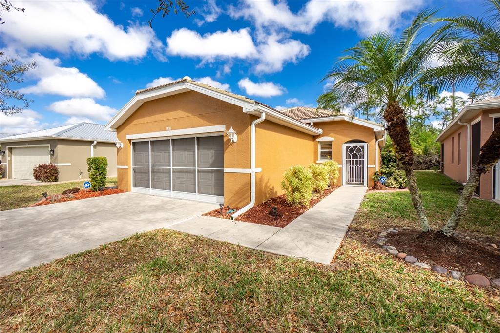 A single-story tan house with a screened garage door, concrete driveway, and a palm tree — 13136 SW PEMBROKE CIRCLE N, LAKE SUZY, FL