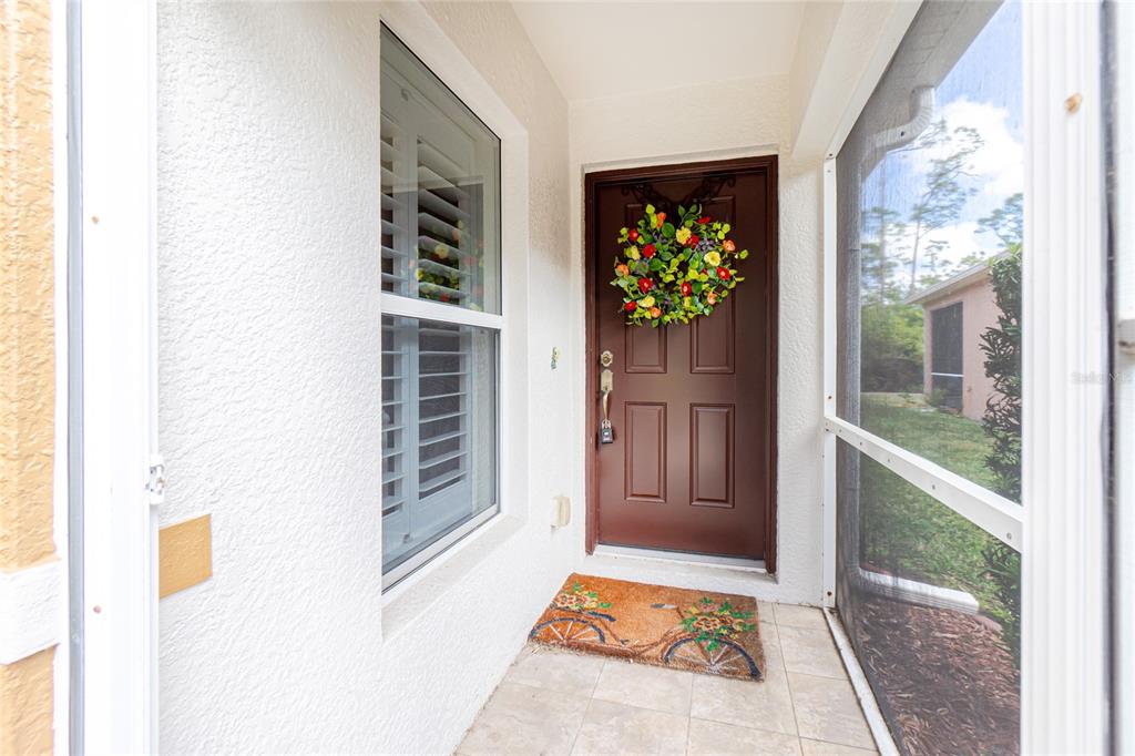 A brown front door with a floral wreath sits on a tiled porch entry — 13136 SW PEMBROKE CIRCLE N, LAKE SUZY, FL