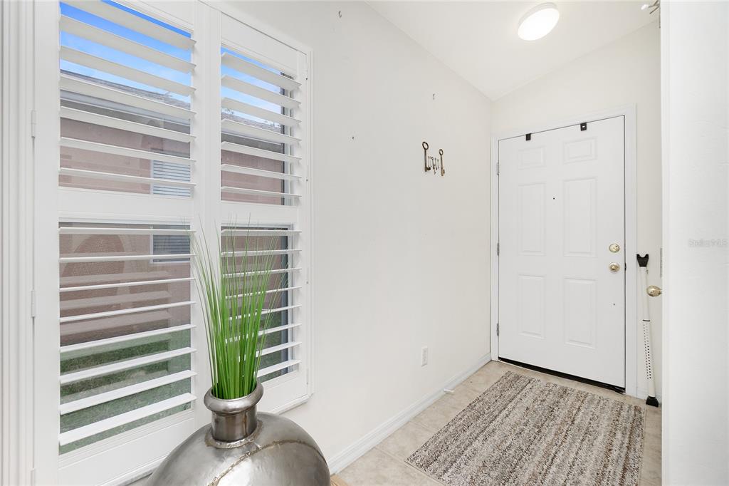 A bright entryway features a white front door, tile flooring, and a window with shutters — 13136 SW PEMBROKE CIRCLE N, LAKE SUZY, FL