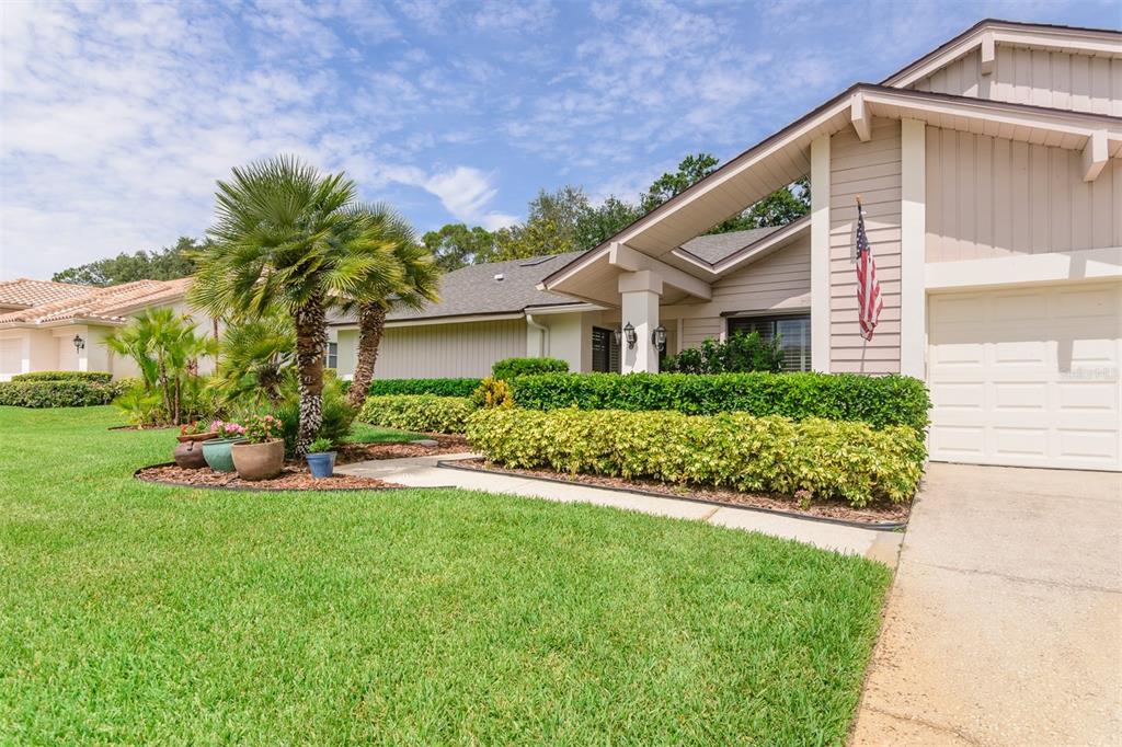 A single-story house with a beige exterior, a white garage door, and a landscaped front yard — 3230 SANDY RIDGE DRIVE, CLEARWATER, FL