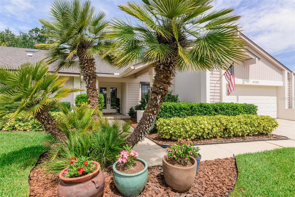 A house exterior features two palm trees, potted plants, and an American flag by the garage — 3230 SANDY RIDGE DRIVE, CLEARWATER, FL