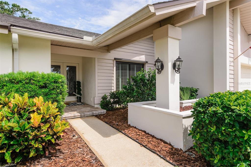 A concrete walkway leads to the covered front entrance of a house with beige siding — 3230 SANDY RIDGE DRIVE, CLEARWATER, FL