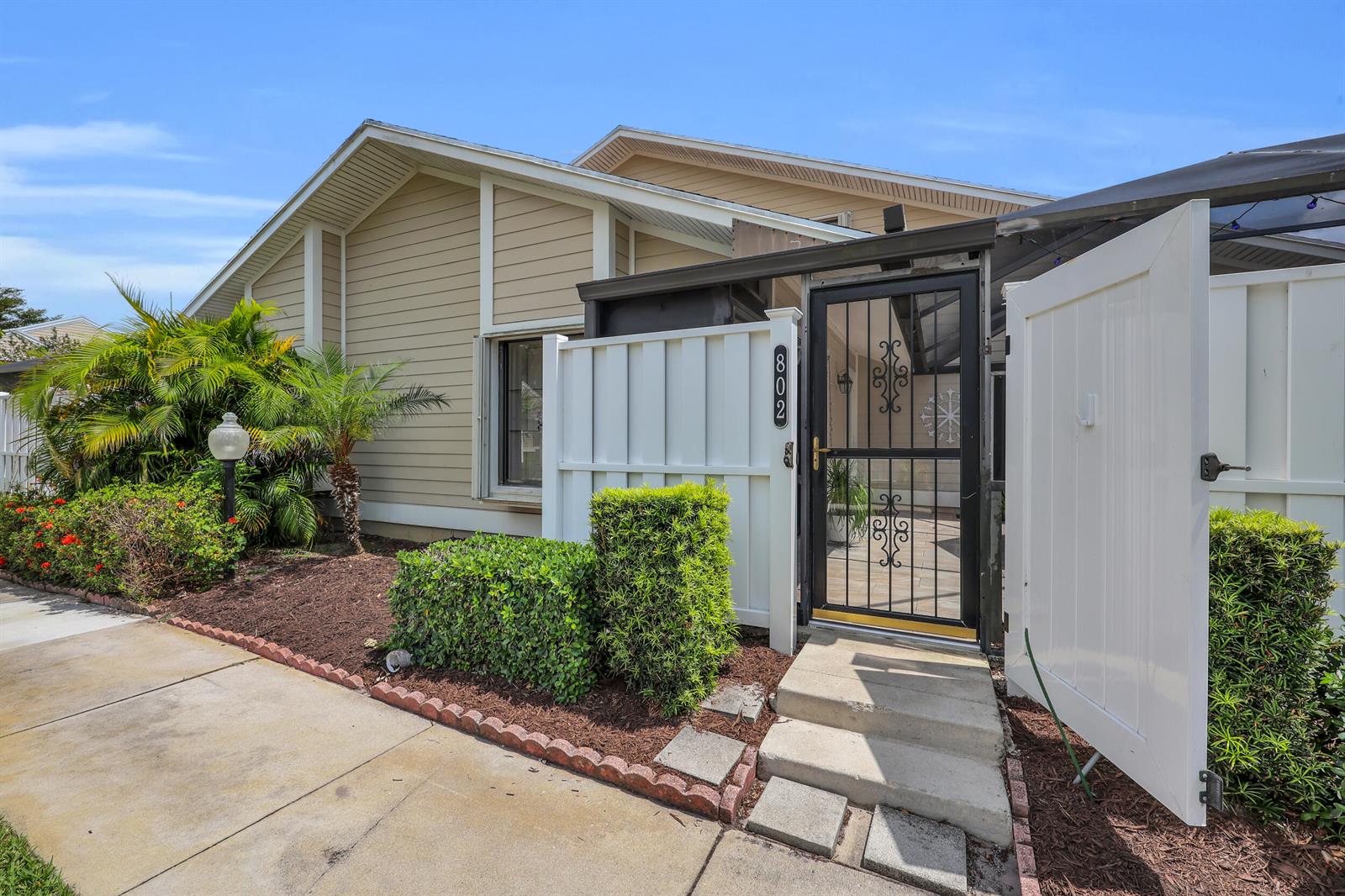 A beige house exterior features a gated courtyard entrance with a screen door and landscaping — 802 Summerwinds Lane, Jupiter FL 33458, JUPITER, FL