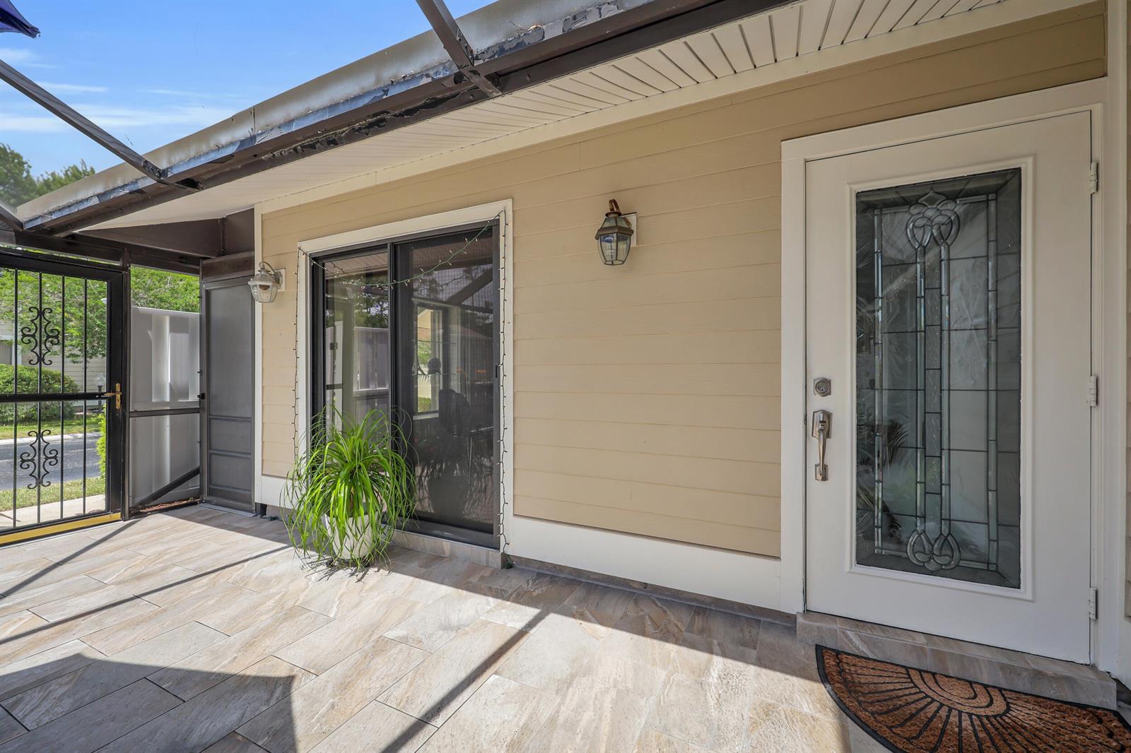 A covered patio features tiled flooring, a sliding glass door, and a decorative front door — 802 Summerwinds Lane, Jupiter FL 33458, JUPITER, FL