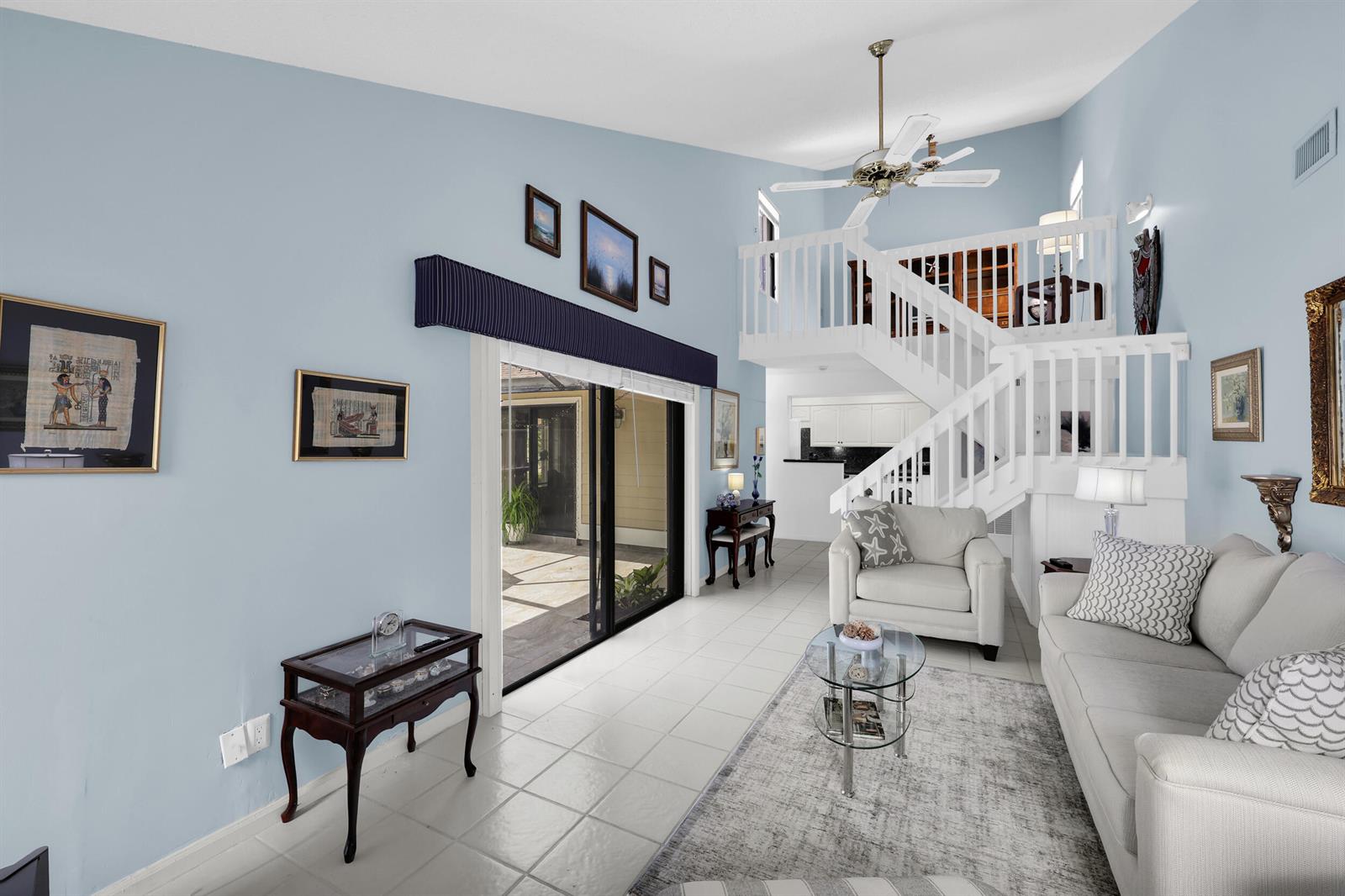 A living room with light blue walls, a white staircase, and a sliding glass door — 802 Summerwinds Lane, Jupiter FL 33458, JUPITER, FL