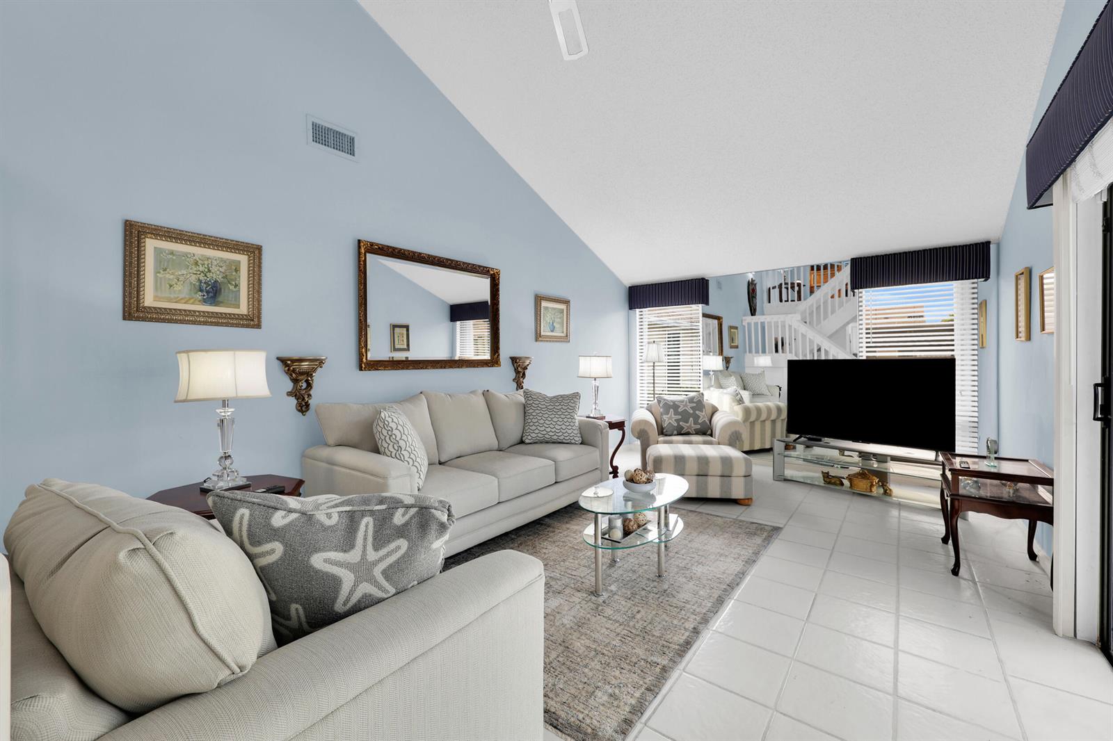 A living room features light blue walls, a vaulted ceiling, tile flooring, and neutral furniture — 802 Summerwinds Lane, Jupiter FL 33458, JUPITER, FL