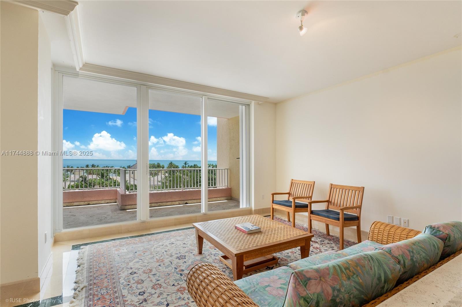A living room features a wicker sofa, wooden chairs, a coffee table, and a balcony view — 785 Crandon Blvd, Key Biscayne FL 33149, KEY BISCAYNE, FL