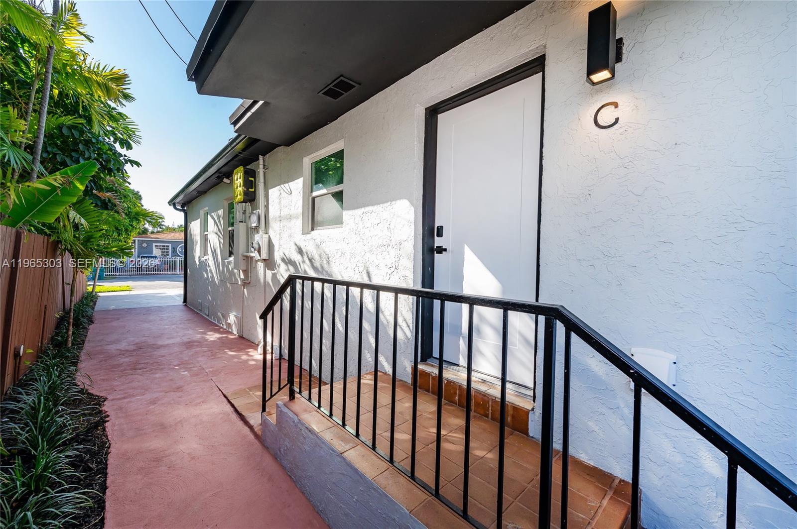An exterior view of a white building entrance labeled C with a black metal railing — 3321 NW 19th Ter # C, Miami FL 33125, MIAMI, FL