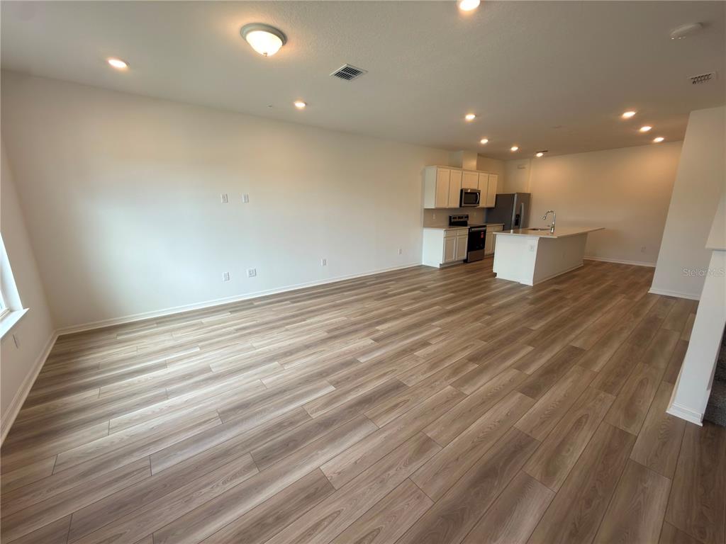 An open-concept living room and kitchen featuring light wood-look flooring and recessed lighting — 11419 HARBORVIEW STREET, ORLANDO, FL