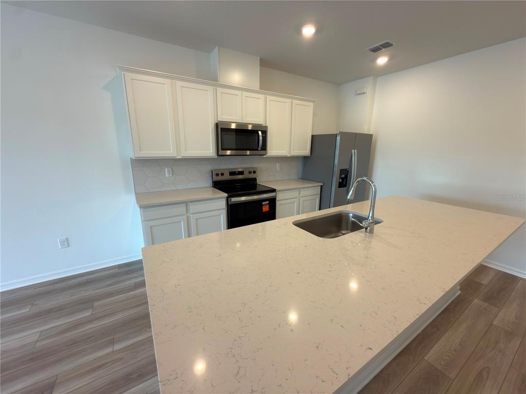A modern kitchen features white cabinets, quartz countertops, a center island, and stainless steel appliances — 11419 HARBORVIEW STREET, ORLANDO, FL
