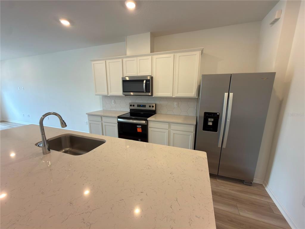 A kitchen features white cabinets, stainless steel appliances, and a large quartz-topped island — 11419 HARBORVIEW STREET, ORLANDO, FL