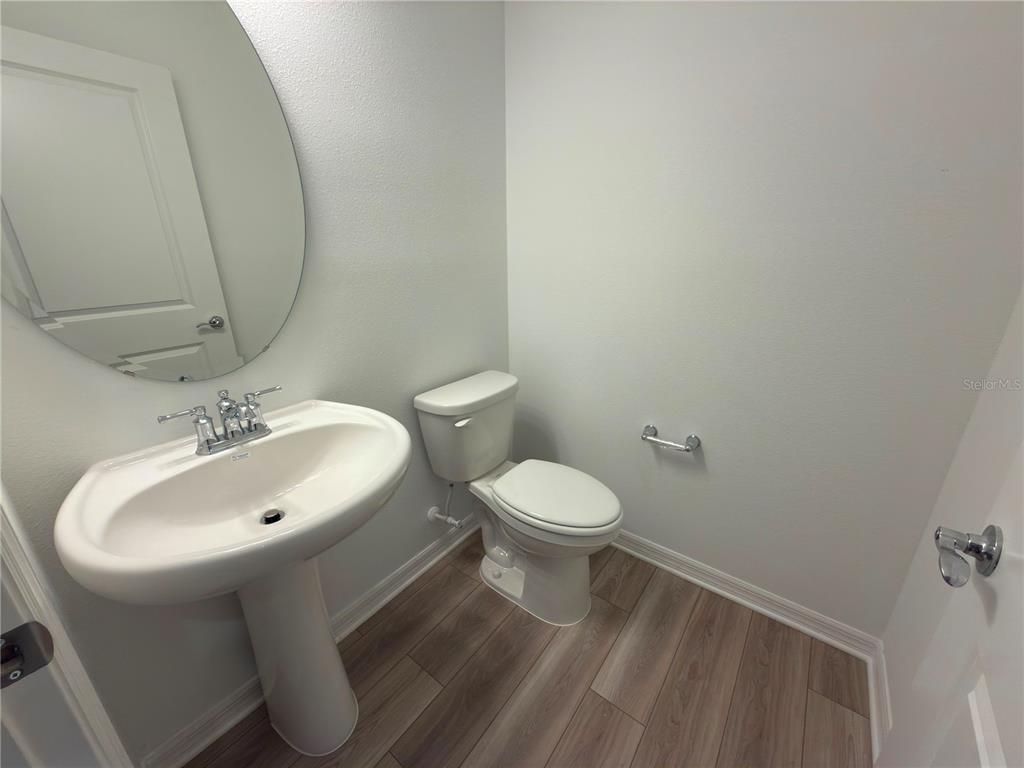A half bathroom features a pedestal sink, a toilet, and wood-look flooring — 11419 HARBORVIEW STREET, ORLANDO, FL