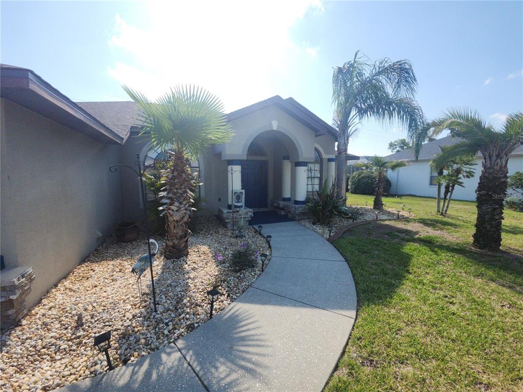 A curved concrete walkway leads to the front entrance of a house with palm trees — 4028 BRECKLAND COURT, SPRING HILL, FL