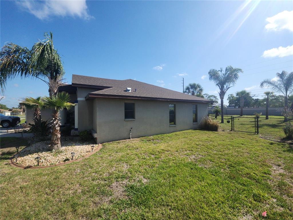 The side exterior of a tan house with a brown roof and a fenced yard — 4028 BRECKLAND COURT, SPRING HILL, FL