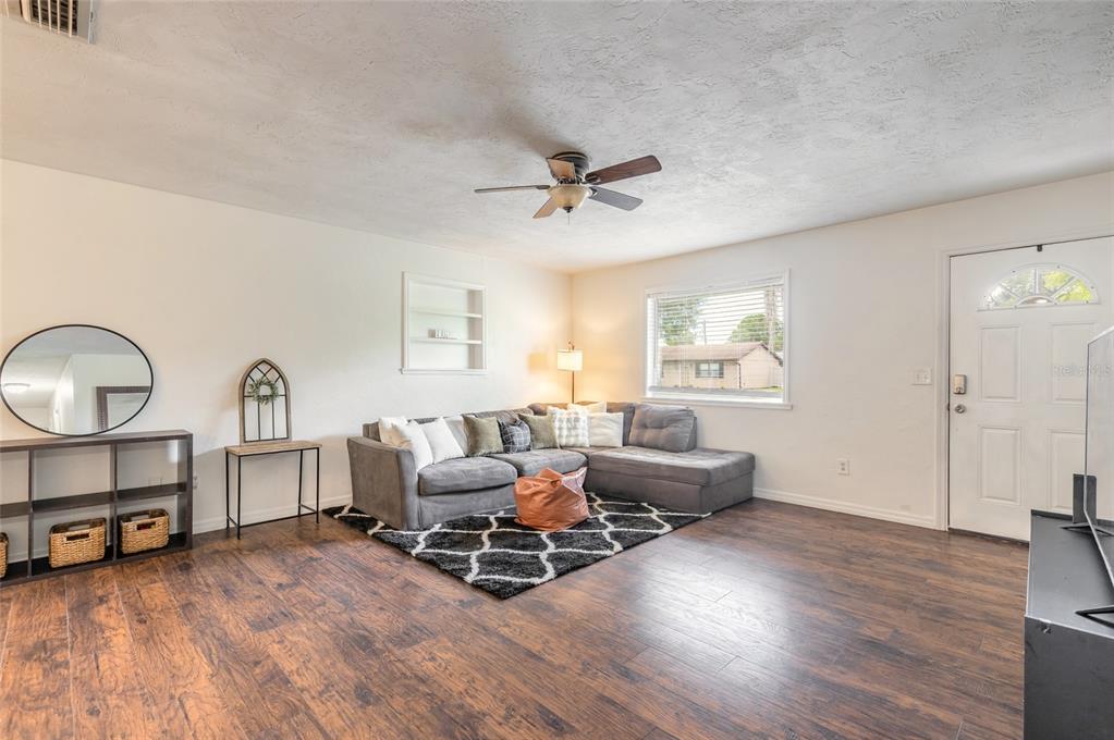 A living room features dark wood flooring, a gray sectional sofa, and a black rug — 3223 UMBRELLA TREE DRIVE, EDGEWATER, FL
