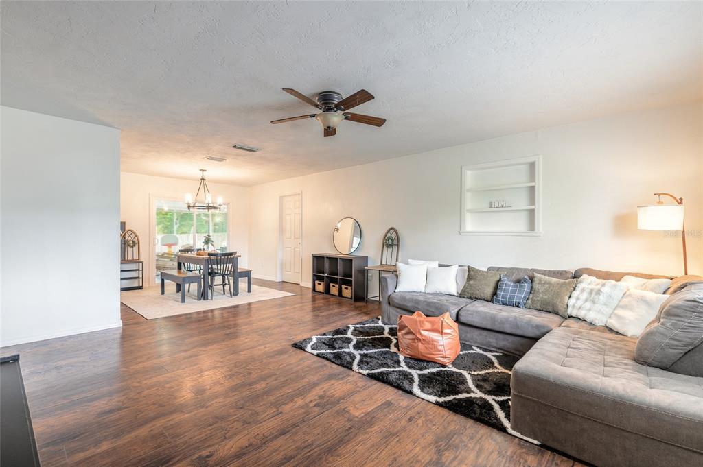 A living room with dark wood floors, a grey sectional, and an adjacent dining area — 3223 UMBRELLA TREE DRIVE, EDGEWATER, FL