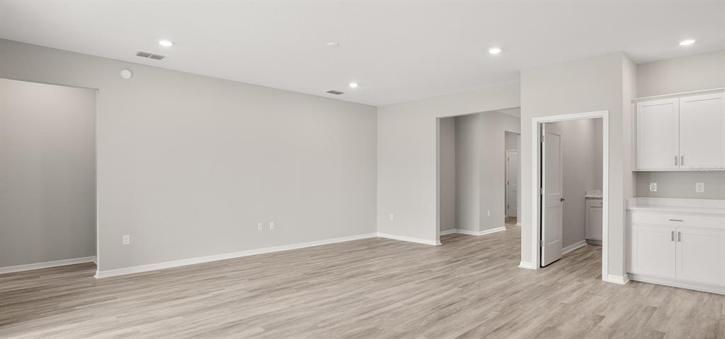A spacious room with light gray walls, wood-look flooring, and a small kitchen area — 7671 SW 6TH LOOP, OCALA, FL