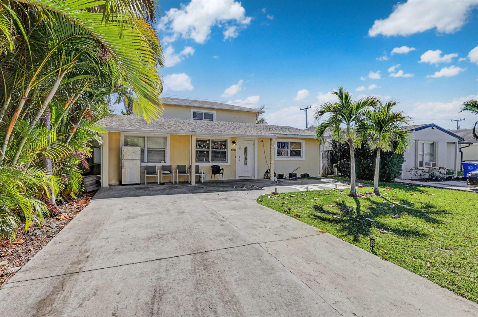 A yellow single-story house with a concrete driveway, palm trees, and a front lawn — 1400 Cardinal Lane, Lantana FL 33462, LANTANA, FL