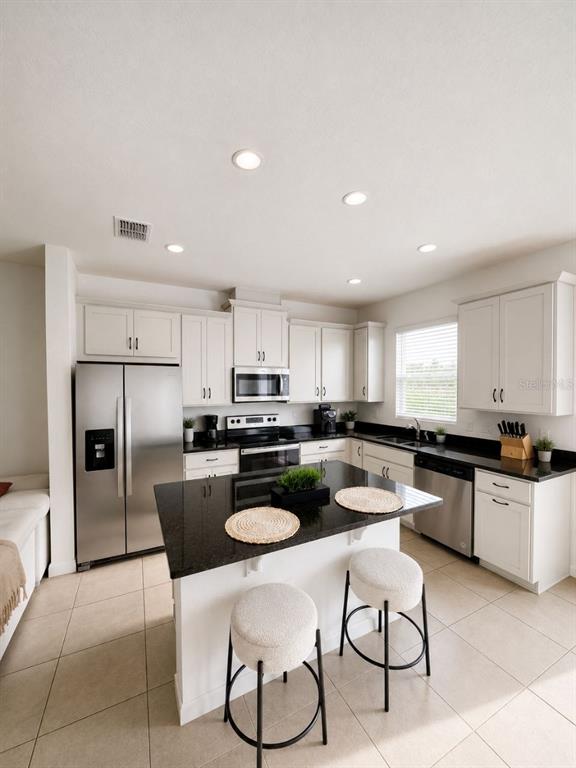 A kitchen features white cabinets, stainless steel appliances, a black island, and light tile flooring — 1190 SEASIDE MIST TRAIL, KISSIMMEE, FL
