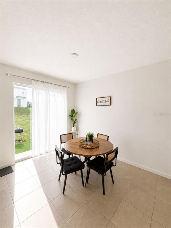 A dining area with a round wooden table, four black chairs, and a sliding glass door — 1190 SEASIDE MIST TRAIL, KISSIMMEE, FL