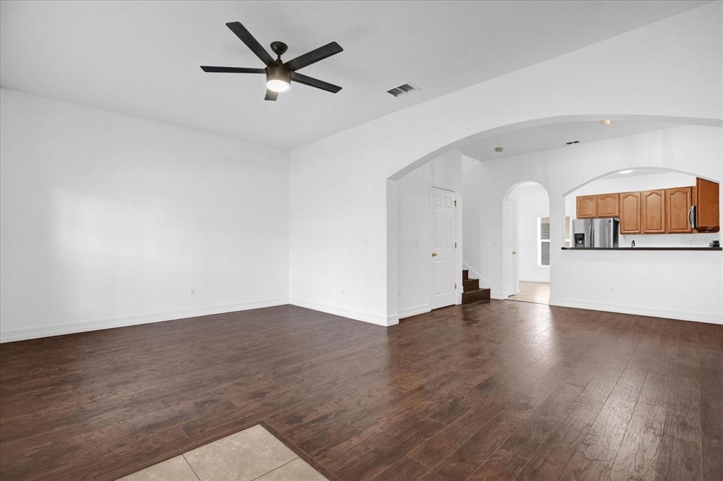 A spacious living room with dark wood-look flooring, a ceiling fan, and an arched entryway — 16130 OLD ASH LOOP, ORLANDO, FL