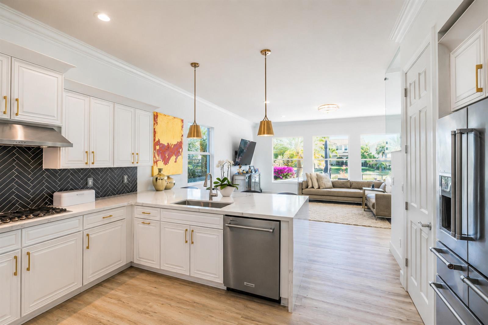 A modern kitchen with white cabinets, gold hardware, and a herringbone backsplash opens to a living room — 11990 NW 83rd Place, Parkland FL 33076, PARKLAND, FL