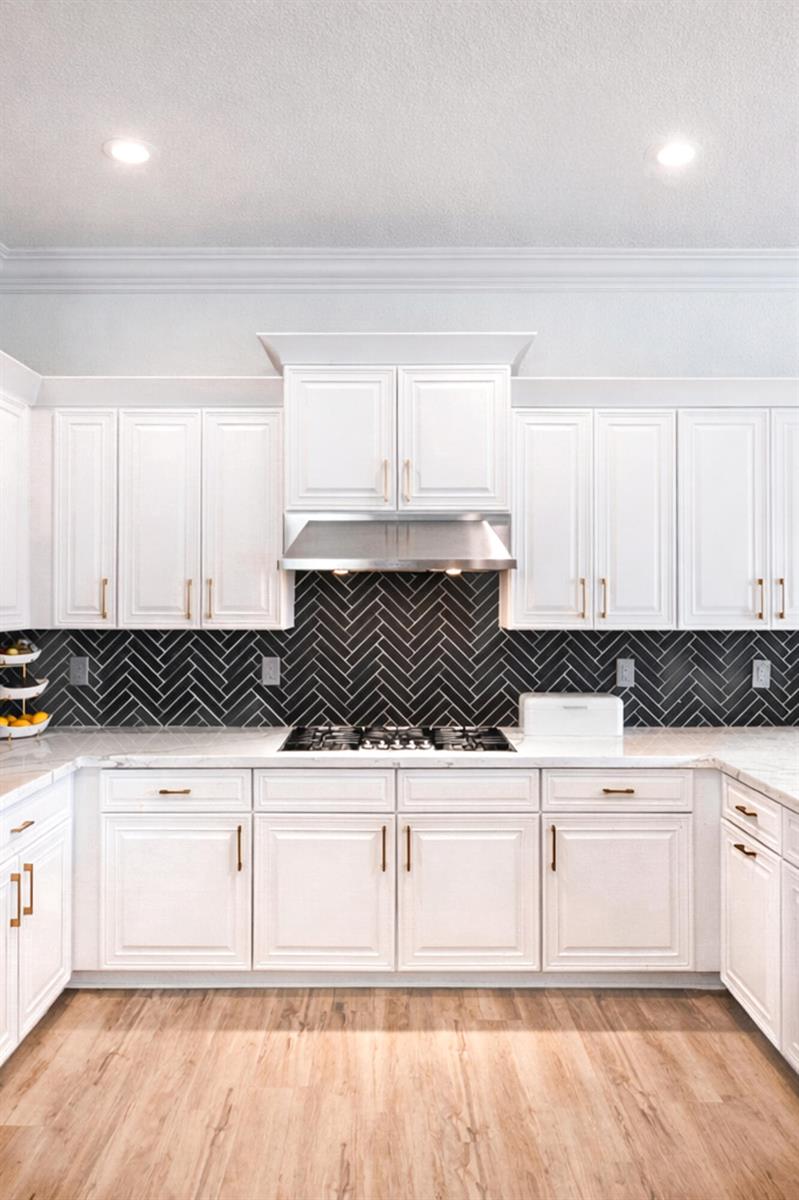 A kitchen features white cabinets, a black herringbone tile backsplash, and light wood flooring — 11990 NW 83rd Place, Parkland FL 33076, PARKLAND, FL