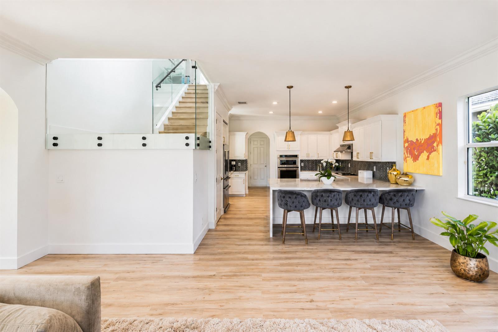 A modern kitchen with white cabinets, a marble island, and bar stools near a staircase — 11990 NW 83rd Place, Parkland FL 33076, PARKLAND, FL