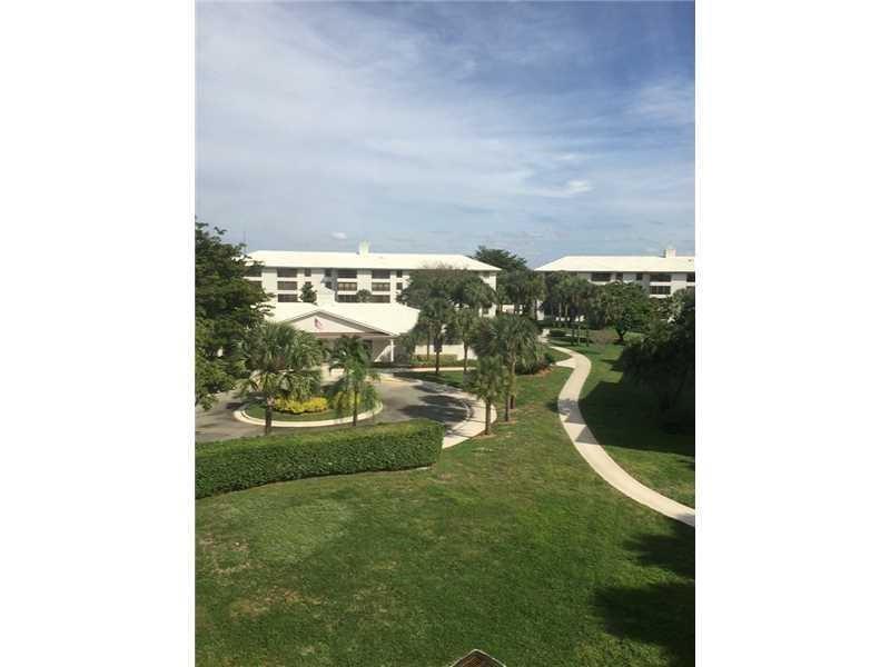 An exterior view of white multi-story apartment buildings surrounded by palm trees and green lawns — 3650 Whitehall Drive # 403, West Palm Beach FL 33401, WEST PALM BEACH, FL